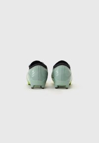 Un paio di scarpe da calcio verde chiaro con accenti neri, dotate di una parte superiore texturizzata, un pannello posteriore liscio e tacchetti sporgenti per una migliore aderenza.