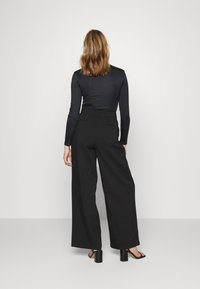 Calças largas pretas com cintura alta, combinadas com uma blusa justa de manga longa preta. Textura suave e design minimalista.