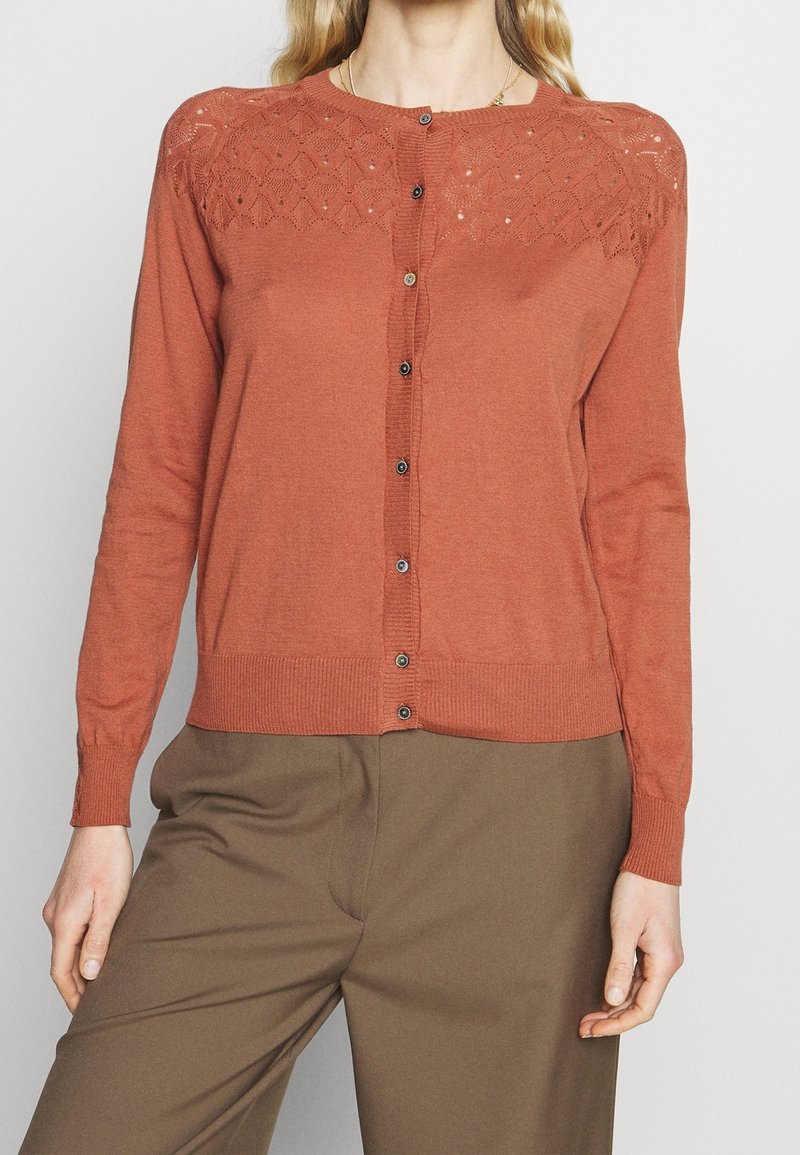 Svetr v rzi s texturovaným vzorovaným průramkem a zapínáním na knoflík. Má dlouhé rukávy a žebrované manžety a lem.