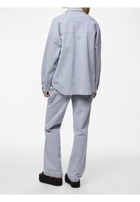 Randig denimskjorta och matchande vida byxor i ljusblått och vitt. Har en lös passform, knappstängning fram och uppvikta ärmar.