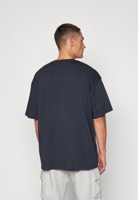 Navy plava oversized majica s kratkim rukavima, okruglim izrezom i glatkom teksturom. Ima jednostavan leđa bez uzoraka ili akcenata.