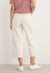 Balti trumpi kelniukai pagaminti iš tvirto audinio, su dviem užpakalinėmis kišenėmis, derinami su baltais sportiniais bateliais ir raudonai baltos dryžuotos marškiniais.