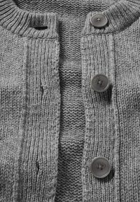 Nahaufnahme eines grauen Strickcardigans mit geripptem Muster, drei grauen Knöpfen und einem Knopfloch am Kragen.