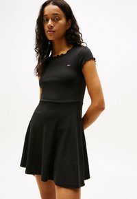 Schwarzes Kurzarmkleid mit tailliertem Oberteil und schwingendem Rock, mit gewellten Kanten an den Ärmeln, aus weichem Baumwollmaterial.