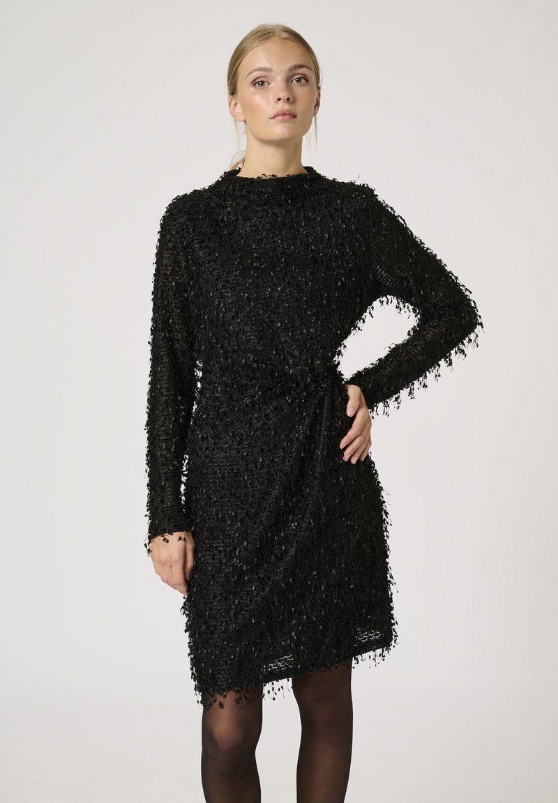 Schwarzes strukturiertes Kleid mit langen Ärmeln und lockerer Passform, ausgestattet mit Fransenverzierungen am Saum und an den Ärmeln sowie einem Twist in der Taille.