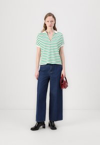 Stripet grønn og hvit kortermet topp med V-hals, parret med høyt liv mørk denim vide ben jeans. Holder en liten rød håndveske.