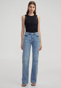 Top negro sin mangas con detalles de encaje y vaqueros de cintura alta en azul claro, con un corte recto y dobladillo deshilachado. Sandalias negras completan el look.