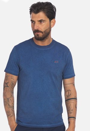 T-shirt blu a girocollo realizzato in un tessuto morbido e texturizzato. Presenta un piccolo logo rosso sul petto. Vestibilità classica con maniche corte.