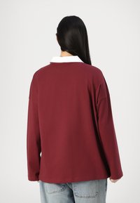 Bordo ilgomis rankovėmis marškiniai su baltu apykakle; laisvas kirpimas; minkšta medžiaga; tiesus apatinis kraštas; šiek tiek nusileidę pečiai; minimalus dekoravimas.