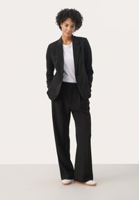 Costume noir ajusté avec un blazer à un bouton et un pantalon large. Associe à un t-shirt blanc et des baskets blanches, créant un look épuré.
