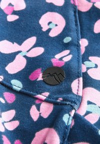 Marinekleurige stof met roze en lichtblauwe bloemenpatronen, voorzien van een zwart, rond logo-label en nette stiksels langs de randen.