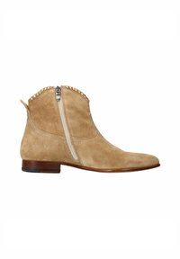 Beige suède enkellaarsjes met een zijrits, vlakke bruine hak en decoratieve metalen accenten langs de rand van de rits.