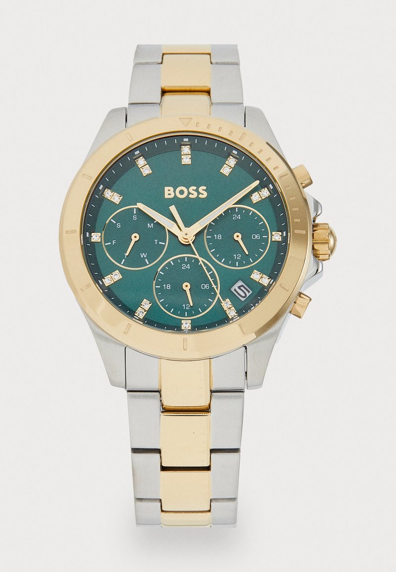 Sidabrinis ir auksinis apyrankinis laikrodis su žalia ciferblatu, chronografo funkcija ir kristaliniais žymekliais. Nebranguose plieno dirželis su poliruotu paviršiumi.