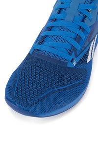 Zilā sporta apava ar teksturētu tīkla augšdaļu, plakaniem šņorēm un gumijas zoli ar noapaļotu pirkstu dizainu. Akcenti ietver baltas detaļas.