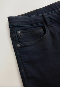 Tmavě modré džínové kalhoty s klasickým designem, stylem s pěti kapsami a kontrastním hnědým štepováním na okrajích a švech.