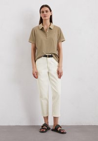Khaki polo shirt met korte mouwen, gecombineerd met witte, cropped broek en zwarte sandalen met een metalen gesp. Eenvoudig, casual ontwerp.