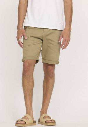 Shorts kaki à revers, fabriqués en tissu léger. Associés à un t-shirt blanc uni et des sandales beiges à enfiler.