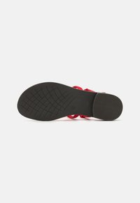 Sandale rouge avec une semelle en caoutchouc noir texturé, dotée de brides entrecroisées et d'un design de semelle plate pour un confort et une stabilité optimaux.