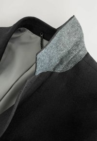 Chaqueta negra con cuello de fieltro gris, que presenta un forro interior suave. El cuello tiene un borde cosido para un detalle adicional.