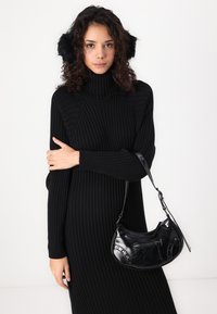Black ribbed knit oversized sweater dress with long sleeves, paired with a black, textured leather handbag featuring metal accents.
