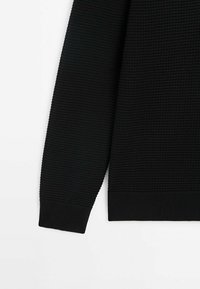 Pull noir avec tissage texturé, poignets et ourlet côtelés, offrant une coupe ample et un col rond, fabriqué en une matière tricot douce.