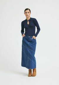 Tengerés ribbelt, hosszú ujjú felső, kulcslyuk nyakkivágással, párosítva egy denim maxi szoknyával, ferde varrással és barna bokacsizmával.