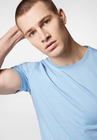 Jasnoniebieska koszulka z krótkim rękawem, uszyta z miękkiego materiału, z okrągłym dekoltem i gładką teksturą. Brak widocznych wzorów czy zdobień.