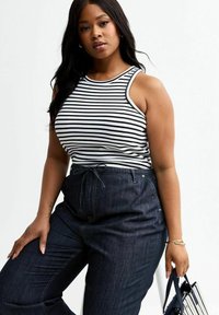 Débardeur rayé en noir et blanc, associé à un pantalon en denim foncé taille haute. Il présente une coupe décontractée et une taille avec cordon de serrage.