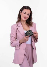 Černá kožená peněženka s texturovaným povrchem a zlatým logem. Držena modelem v růžovém obleku. Zaměření na elegantní design a kompaktní tvar.