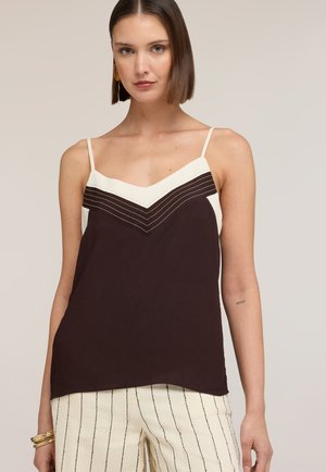 Kvinde med kort brunt hår iført en sort og hvid ærmeløs top med tynde stropper og hvide bukser med lodrette sorte striber.