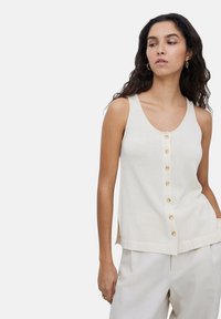 Top sin mangas color beige con frente de botones, que presenta botones redondos, un escote redondeado y aberturas laterales para facilitar el movimiento.