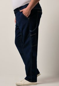 Pantalones de mezclilla de un azul oscuro con un ajuste relajado, que presentan costuras en contraste, bolsillos laterales y una textura suave, combinados con zapatillas blancas.