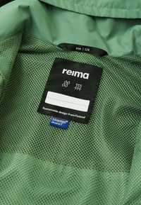 Green jacket interior featuring a mesh lining. Labels indicate size 128, brand "Reima," and "bluesign" certification for sustainable design.