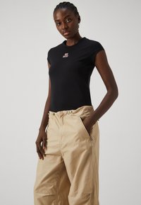 Svart tettsittende t-skjorte med korte ermer, med en sentral rosa "DIESEL" logo. Beige cargo-bukser med elastisk midje og sidelommer.