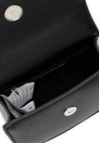 Interior de una cartera de cuero negro que presenta una textura suave, cierre de botón a presión plateado y etiquetas de producto visibles con instrucciones de cuidado.