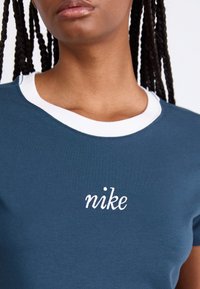 Σκούρο μπλε μπλουζάκι με λευκό γιακά, διακοσμημένο με κεντημένο λογότυπο "nike" σε λευκό χρώμα. Φτιαγμένο από αδιάβροχο ύφασμα, με κοντά μανίκια.