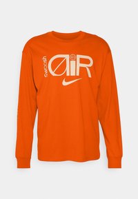 Orange long-sleeve t-shirt made of cotton with printed black "swoosh" and "AIR" text, featuring a basketball graphic and ribbed cuffs.