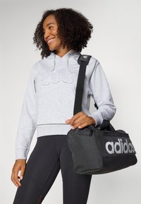 Grijze hoodie met textuurlogo, zwarte sporttas met grote witte merknaam, strak ontwerp en verstelbare schouderriem.
