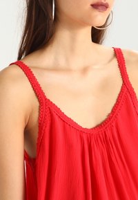 Haut sans manches rouge avec une finition texturée, doté d'un délicat bord en dentelle le long du col et des bretelles, et d'une coupe ample et fluide.