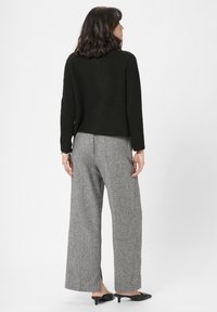 Sort strikket sweater, grå brede mønstrede bukser og sorte slip-on sko. Tøjsettet har et afslappet design og tekstureret stof.