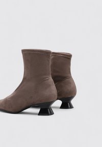 Bottes de cheville en daim marron avec un haut ajusté et un talon évasé noir unique, présentant des lignes épurées et des détails de couture subtils.