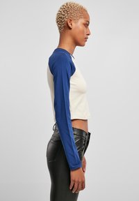 Langarm, cropped top met marineblauwe mouwen en een lichtcrème lijf. Gemaakt van zachte katoen met een getailleerd ontwerp en geribbelde manchetten.