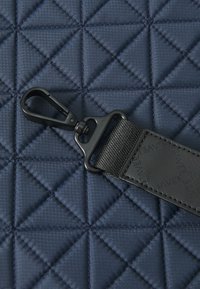 Kvadrični tamnoplavi materijal s dijamantnim uzorkom, koji sadrži crnu kopču i teksturirani remen s utisnutim brendingom.