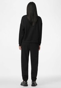 Czarny komplet dresowy, składający się z bluzy i spodni, o luźnym kroju i elastycznych mankietach, wykonany z miękkiego materiału. Dopełnieniem stroju są czarne buty sportowe.