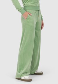 Pantalons de survêtement en velours vert avec une coupe décontractée, dotés de poches latérales et d'une taille à cordon. Associés à des baskets blanches et grises.