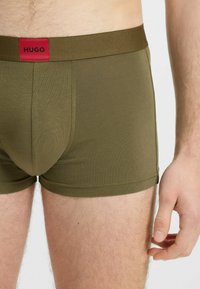 Boxer da uomo verde oliva con una consistenza morbida, dotati di un elastico solido con la scritta "HUGO" in rosso. Vestibilità elegante, design a lunghezza ginocchio.