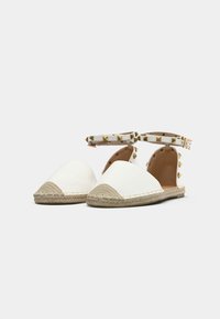 Weiße Espadrille-Flachschuhe mit spitzer Zehenform, ausgestattet mit einer strukturierten, natürlichen Jutesohle und einem Knöchelriemen, der mit goldenen Nieten verziert ist.
