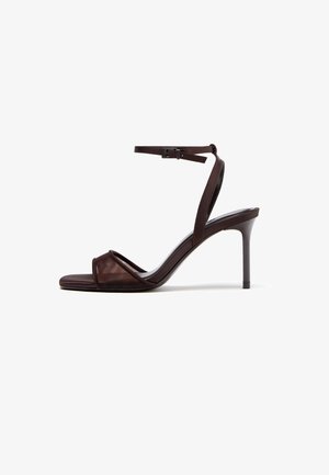 Mørkebrune sandaler med høje hæle, tynd ankelrem og åben tå, med krydset frontbånd og stiletthæl.