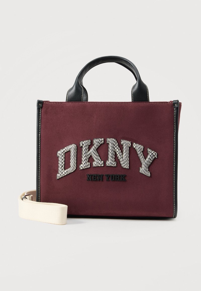 Sac à main rectangulaire bordeaux avec poignées noires, bandoulière blanche amovible et logo texturé "DKNY New York" sur le devant.