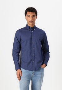 Navyblauw overhemd met knopen, voorzien van kleine witte stippen, een kraag en lange mouwen. Gecombineerd met lichtblauwe denimjeans.